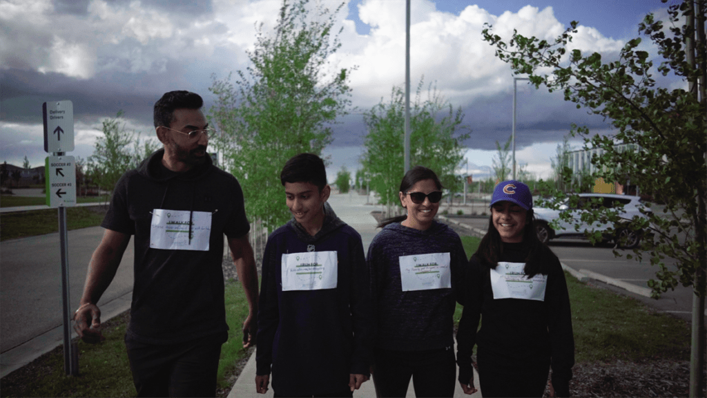 A family of 4 smiling and walking on a sidewalk