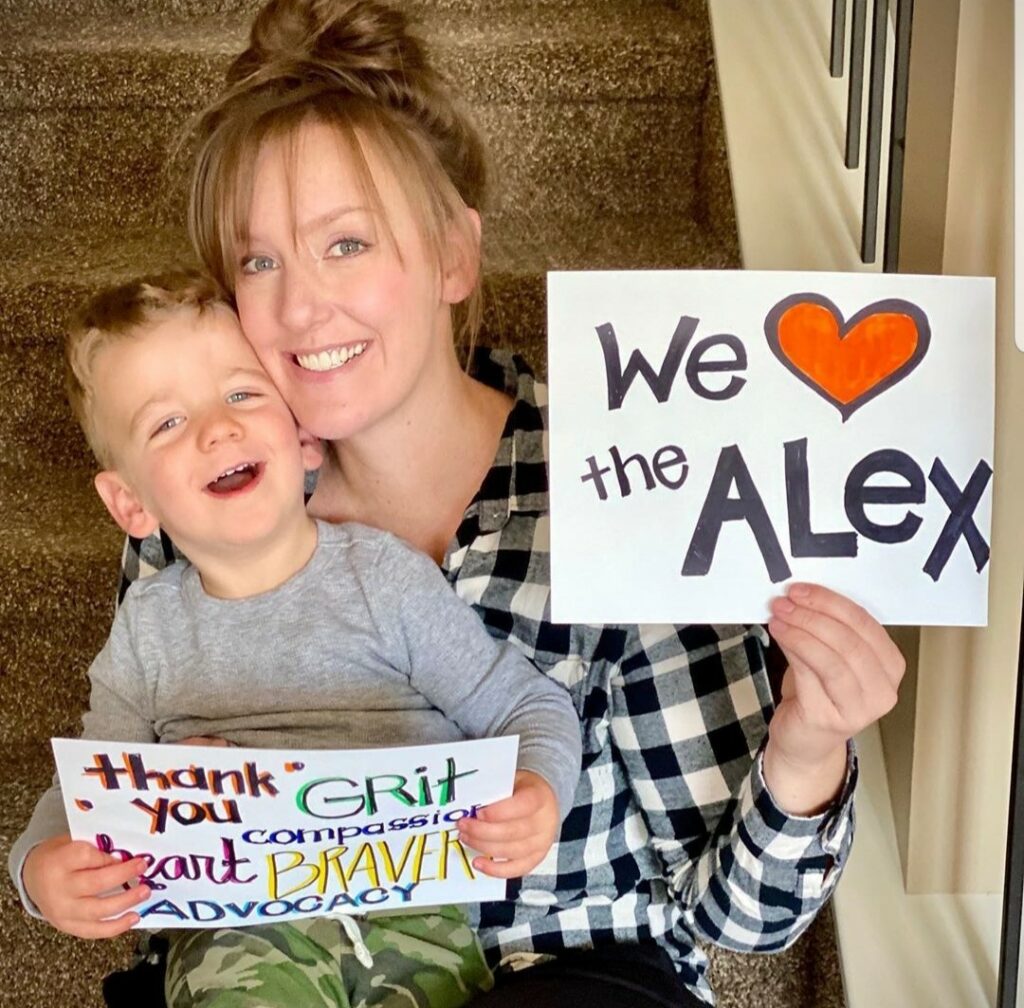 Mother and child holding signs that say "We love The Alex"