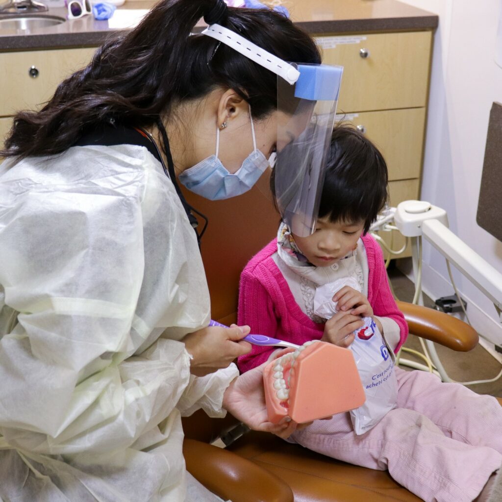 dental hygenist teaching a child how to brush properly using a model of teeth